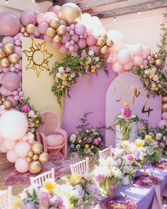 a table set up for a party with balloons and flowers on the wall behind it