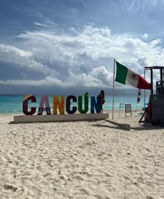 a sign that reads cancun on the beach with people in the water behind it