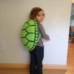 a little boy standing next to a wall with a stuffed turtle on it's back