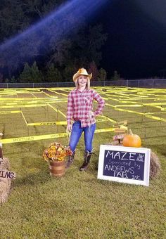 a woman standing next to two hay bales with pumpkins on them in front of a maze