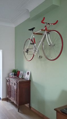 a bicycle mounted to the side of a green wall next to a wooden cabinet and table