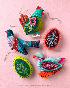 four colorful birds are hanging on a pink wall and one is made out of fabric