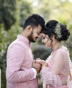 a man and woman standing next to each other in front of trees with their hands together