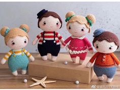 crocheted dolls are standing on a wooden block with starfish nearby, and one is holding the other's hand