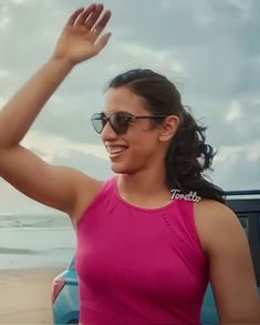 a woman in a pink tank top waves to the sky