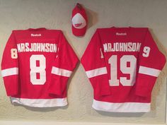 two red hockey jerseys are hanging on the wall next to a baseball cap and hat