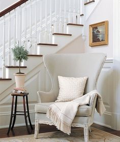 a white chair sitting in front of a stair case next to a table with a potted plant on it