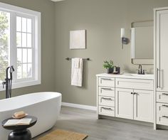 a white bath tub sitting next to a bathroom sink under a window with two mirrors