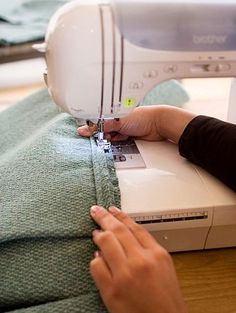 a woman is using a sewing machine to sew on a piece of cloth with her hands