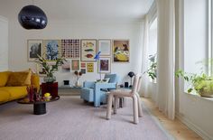 a living room filled with furniture next to a window covered in plants and pictures on the wall