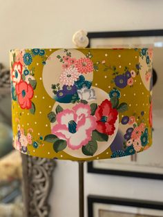 a lamp shade with flowers on it in front of a mirror and framed pictures behind it