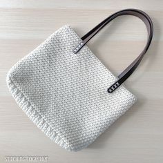 a white knitted bag sitting on top of a wooden table next to a black handle