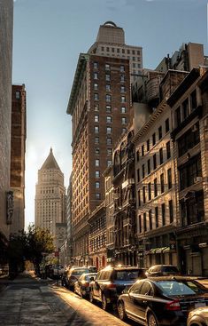 a city street with cars parked on both sides and tall buildings in the back ground