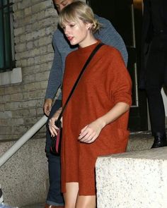 a woman in an orange sweater is walking down the stairs with her hand on her hip