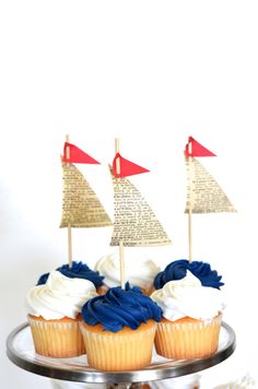 cupcakes decorated with sailboats and blue icing on a silver cake plate