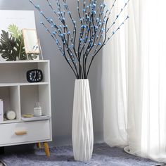 a white vase with blue flowers in it next to a book shelf and window sill