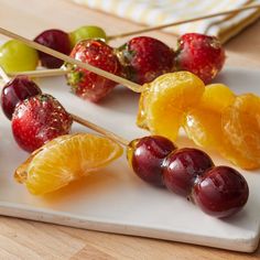 oranges, cherries and strawberries are arranged on a white cutting board with wooden skewers