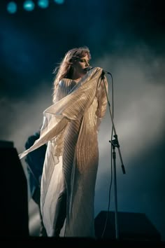 a woman standing on top of a stage with a microphone in her hand and wearing a white dress