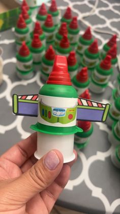 a hand is holding a small toy rocket with red and green caps on it's top