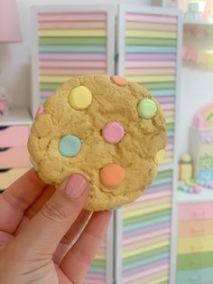 a hand holding a cookie with pastel dots and candy on it's side