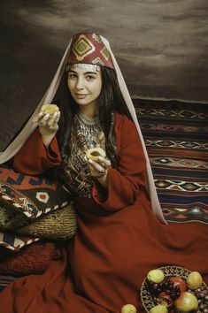 a woman sitting on the floor with food in her hand and wearing a headdress