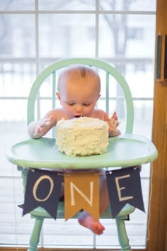 a baby sitting in a high chair with a cake on it's table and the first one is out