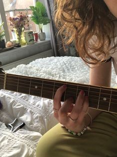 a woman sitting on top of a bed holding an acoustic guitar in her hand and looking down at the strings