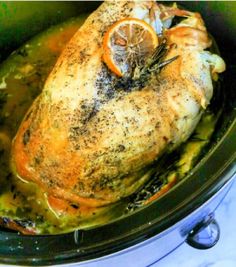 a cooked chicken in a slow cooker with lemons and herbs on top, ready to be eaten