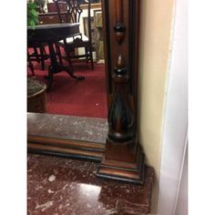 an old grandfather clock is standing in front of a mirror on the floor next to a table