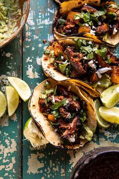 three fish tacos with lime wedges and guacamole on the side