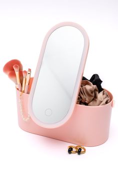 a pink vanity mirror with makeup brushes and other items in the container next to it