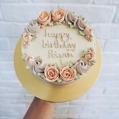 a birthday cake with frosting and flowers on it is being held by a person's hand