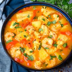 a blue bowl filled with shrimp and vegetable soup next to cilantro, parsley