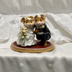 a figurine of two mice dressed in wedding attire and holding each other's hands