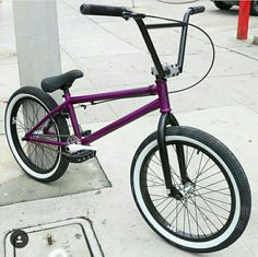 a purple bike parked on the sidewalk next to a pole