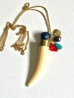 A brass mounted resin animal tooth hangs alongside a turquoise nugget, a dark blue chalcedony stone, red coral, black pearl and a brass sun charm. The pendant is roughly 3.5 inches long. The chain is belcher style in matte gold plated brass and is 36 inches long. Unique Brass Charm Necklaces, Unique Brass Pendant Charm Necklaces, Unique Brass Pendant Charm Necklace, Tooth Pendant, Animal Teeth, Sun Charm, Chalcedony Stone, Clover Necklace, Green Quartz