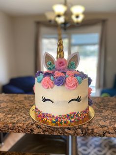 a birthday cake decorated with sprinkles, flowers and a unicorn's face