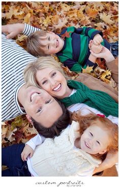 three adults and two children laying on the ground with leaves in front of their faces