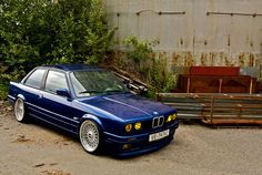 a blue bmw is parked in front of some bushes