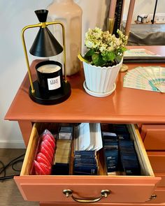 an open drawer with books and flowers on it next to a lamp, mirror and other items