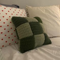 a bed topped with lots of pillows covered in green and white blankets next to each other