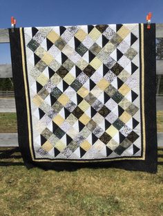 a black and white quilt is hanging on a wooden fence in front of some grass