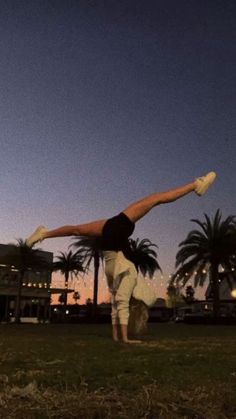 a man doing a handstand on top of a grass covered field next to palm trees