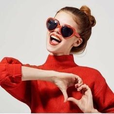 a woman in red sweater and sunglasses making the shape of a heart with her hands