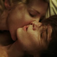 two people laying in bed with one kissing the other's cheek while the other sleeps