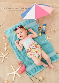 a baby laying on top of a blue towel next to an umbrella and starfish