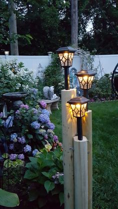 some lights that are sitting in the grass near bushes and flowers on a fence post