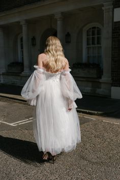 a woman in a white dress is walking down the street with her back to the camera