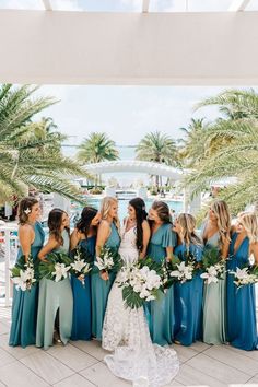 a group of women standing next to each other in front of palm trees and water