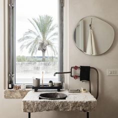 a bathroom sink sitting under a large window next to a potted plant and mirror